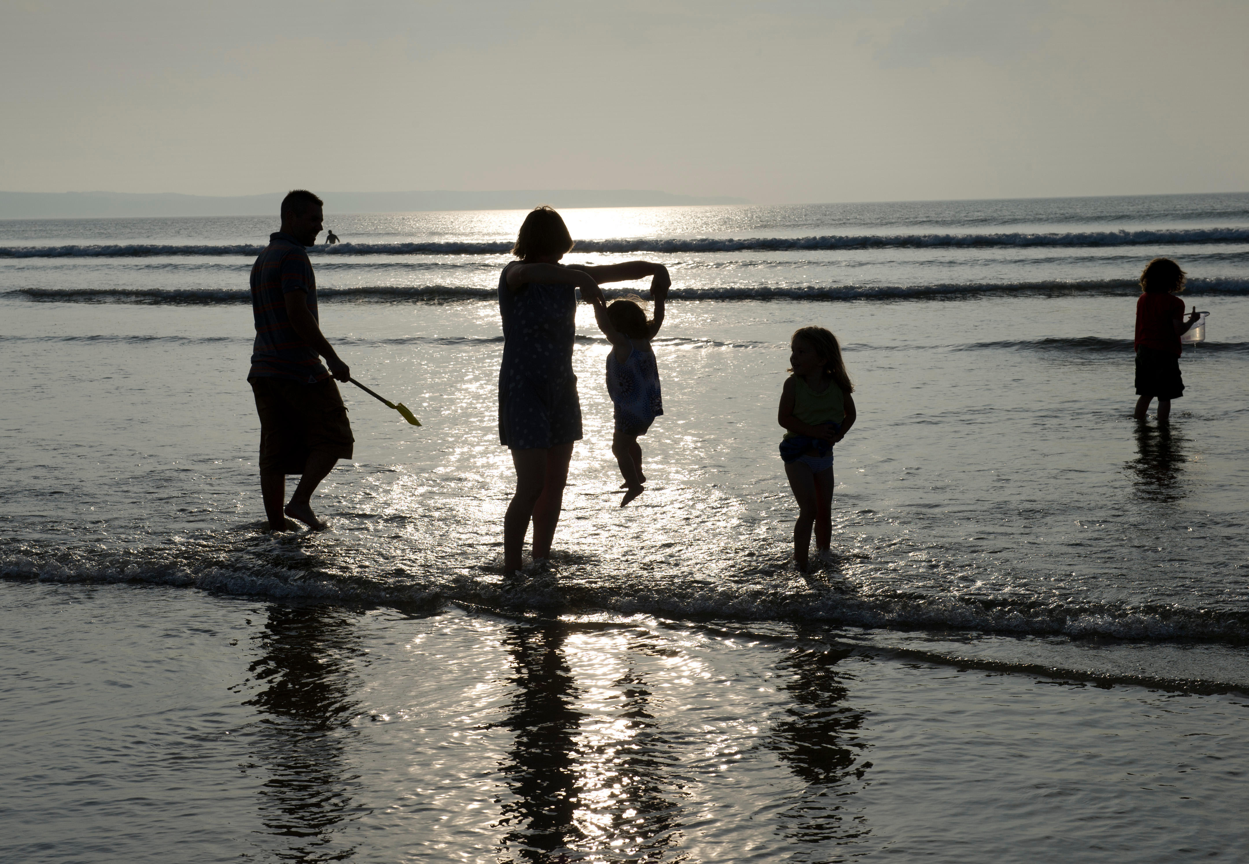 A family of five paddling in the sea at sunset, on the beach.