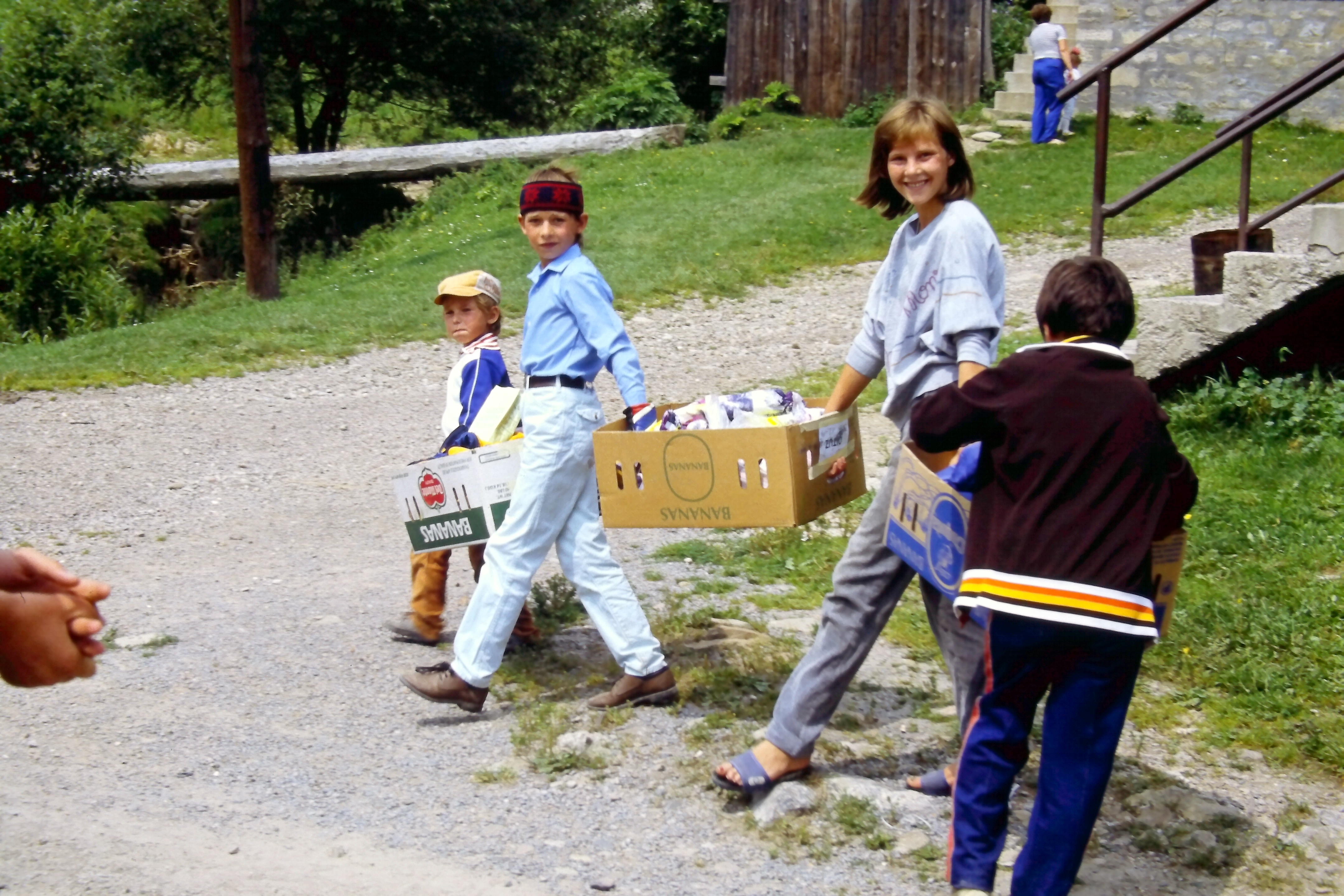 Kinder tragen Pappkartons auf einem Weg im Freien.