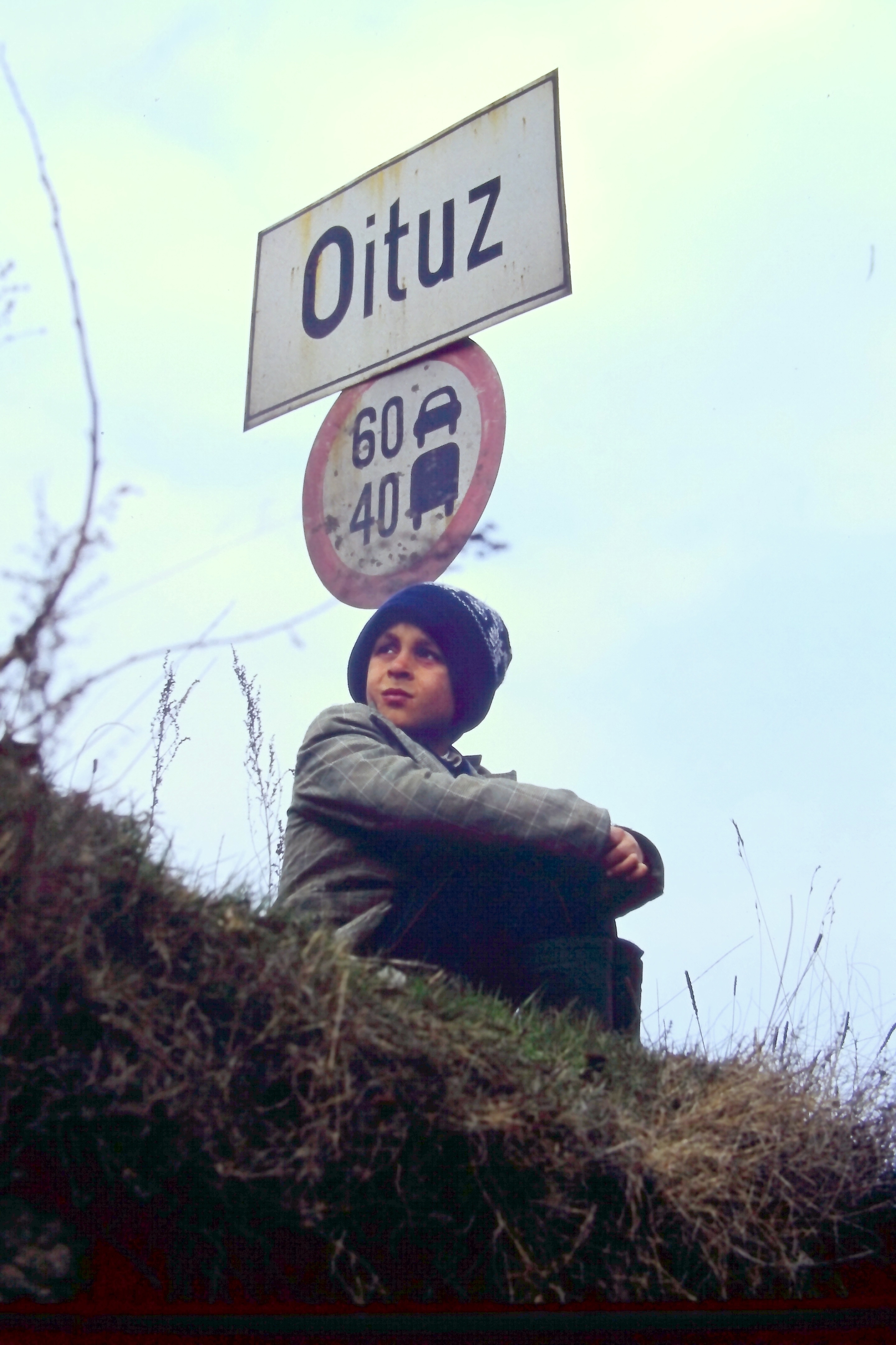 Eine Person sitzt unter Verkehrsschildern mit der Aufschrift „Oituz“ und der Geschwindigkeitsbegrenzung in einer ländlichen Gegend.