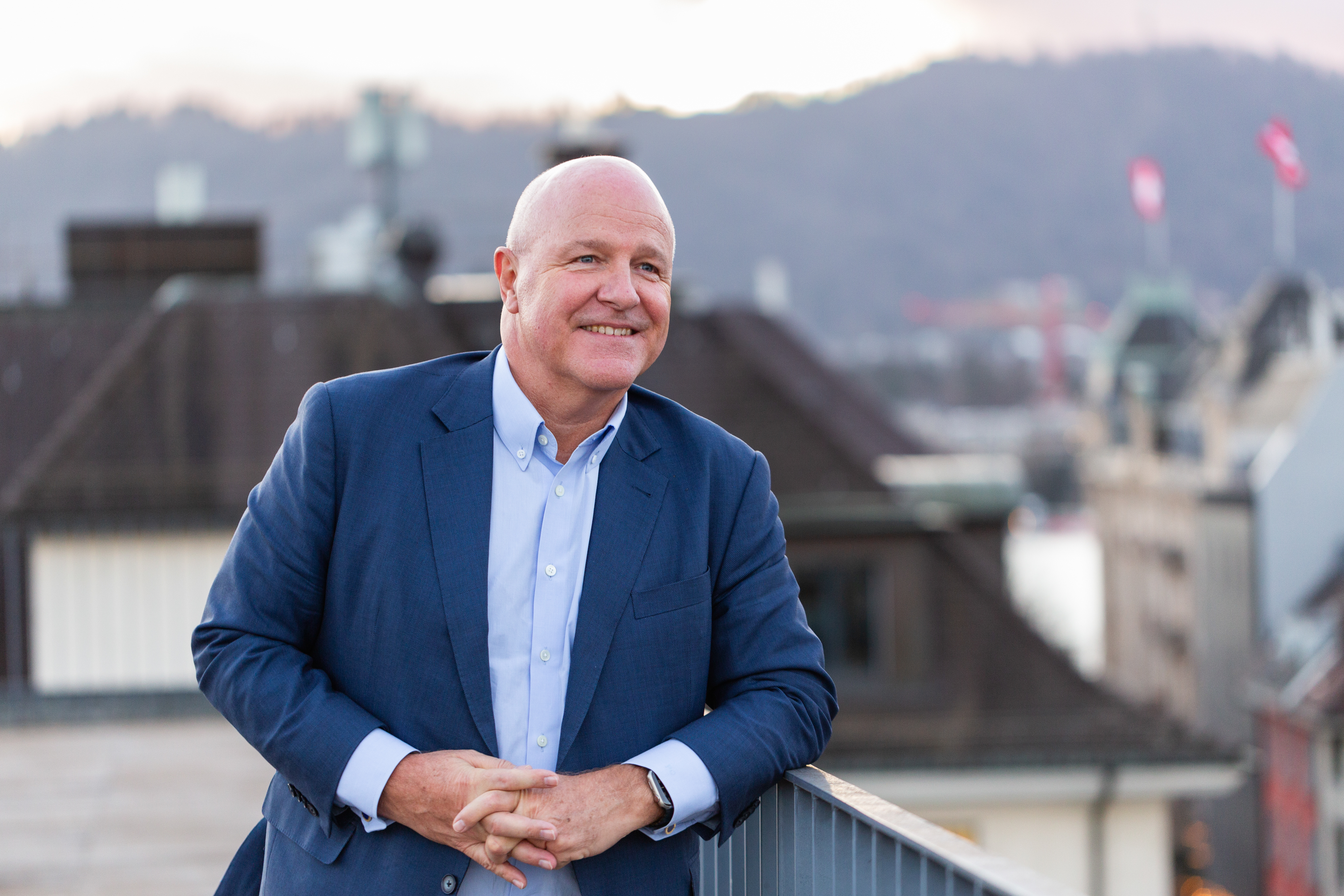 Peter Ohnemus smiles while leaning on a railing with a cityscape in the background.