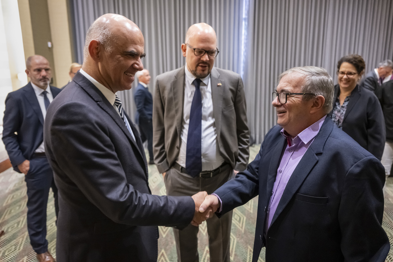 Homens reunidos e uma sala. Um aperta a mão do outro.