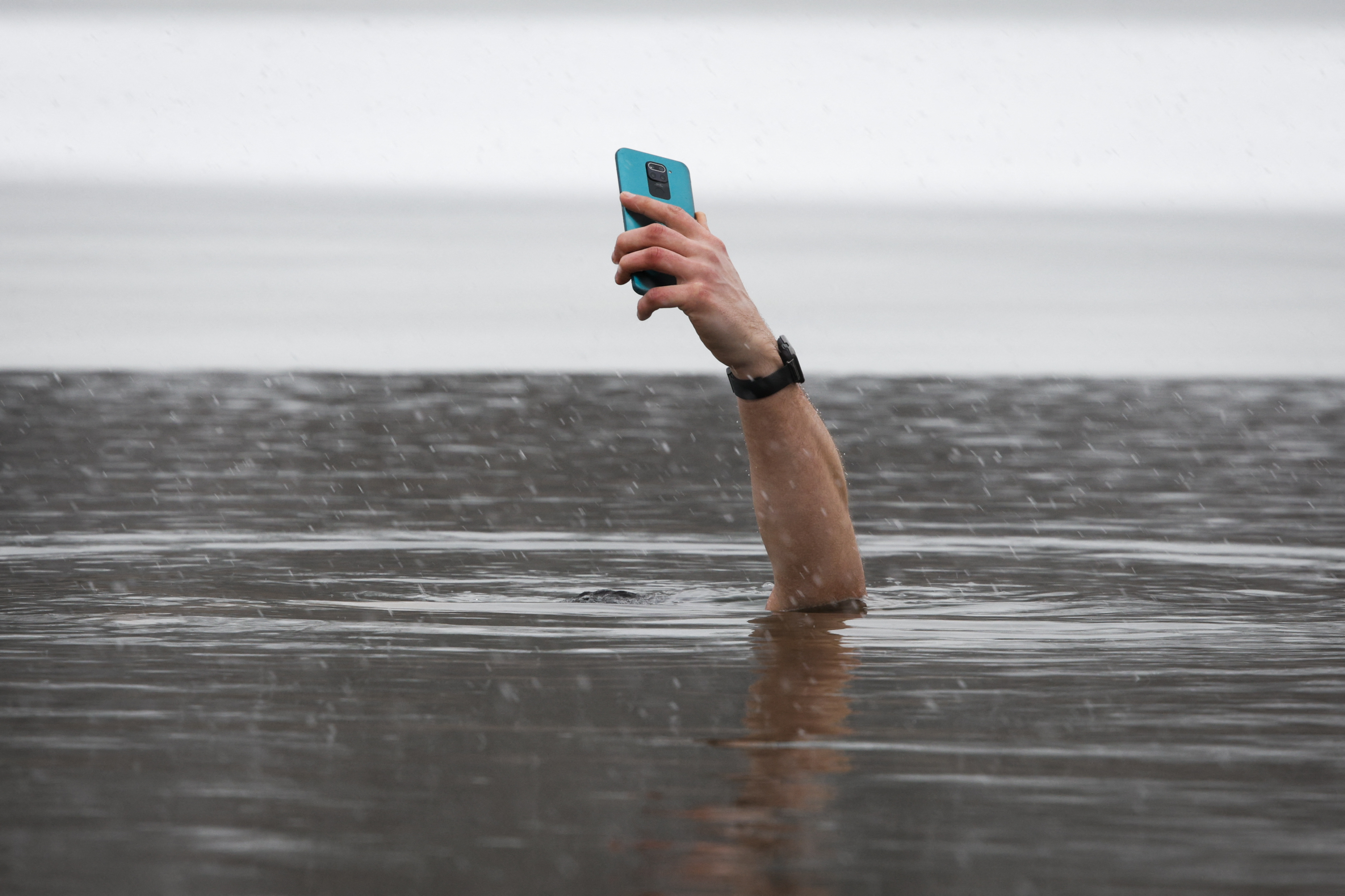 Ein Arm ragt aus dem Meer und hält ein Handy in der Hand