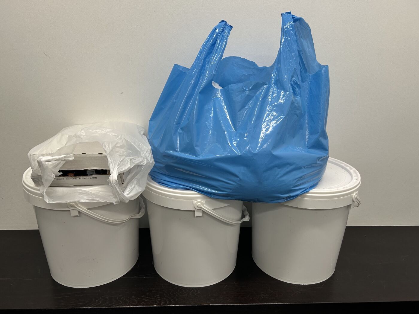 tre bidoncini in plastica bianca e un sacchetto blu