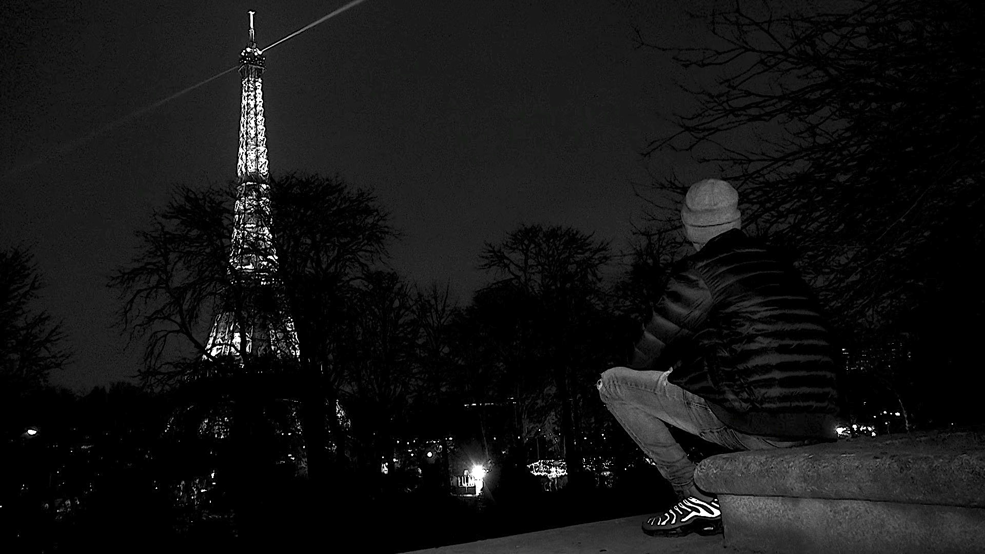 Un jeune vu de dos regarde la tour Eiffel dans la nuit.