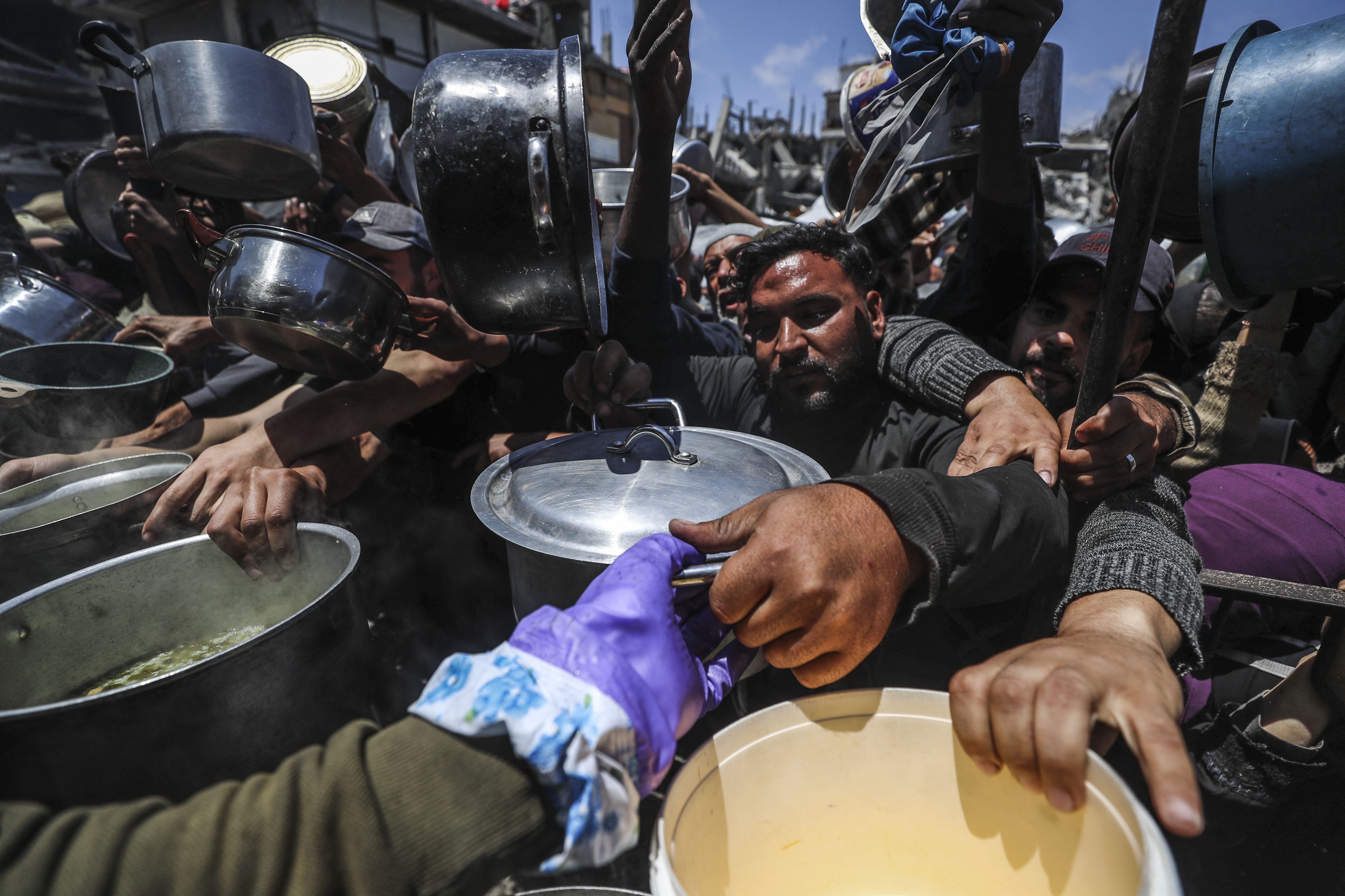 Palestinians, including children, who are struggling with hunger wait in line to receive hot meals distributed by charity organizations.