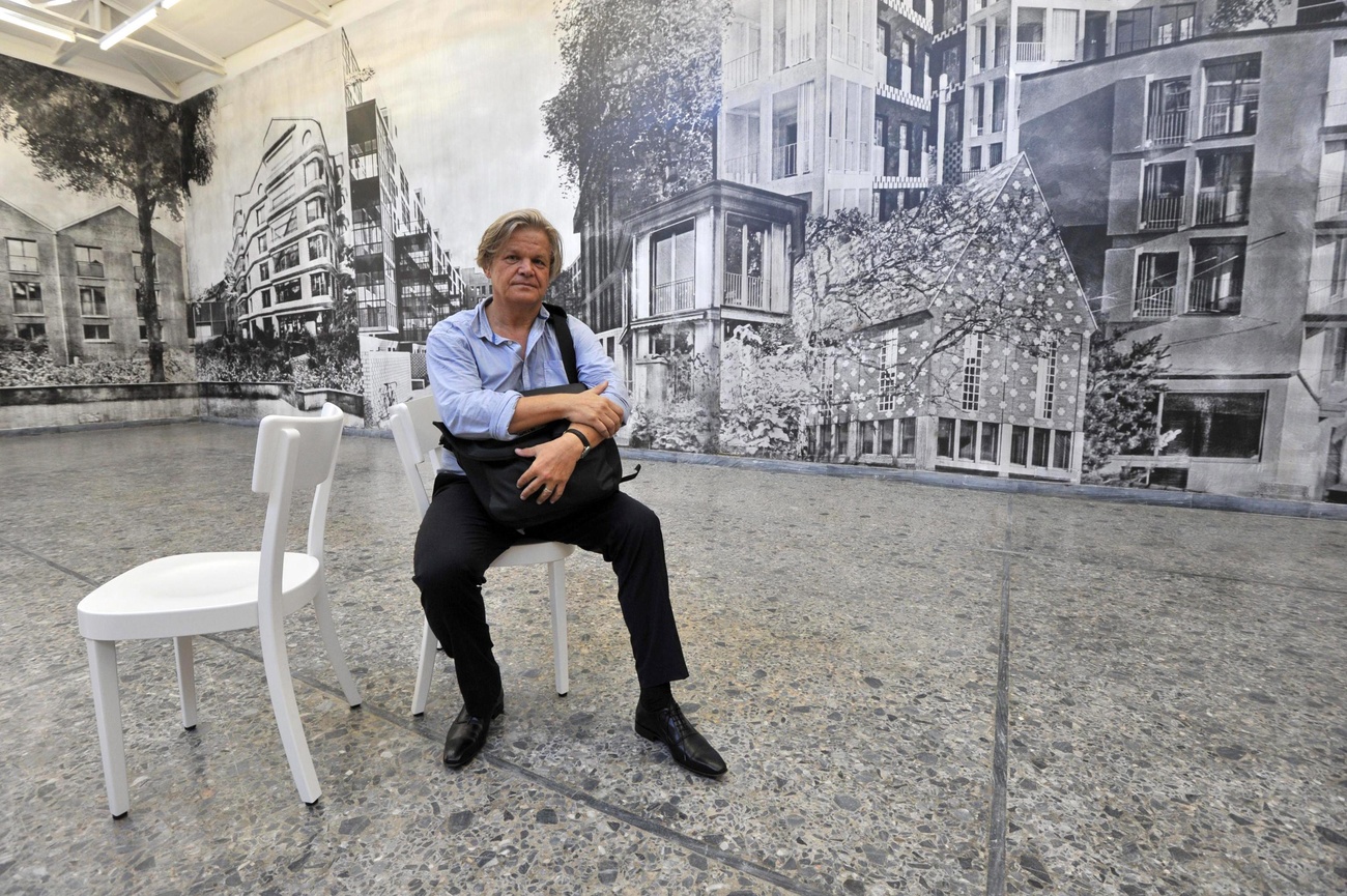 Ein Mann auf einen Stuhl vor einer Schwarzweiss-Collage verschiedener Gebäude