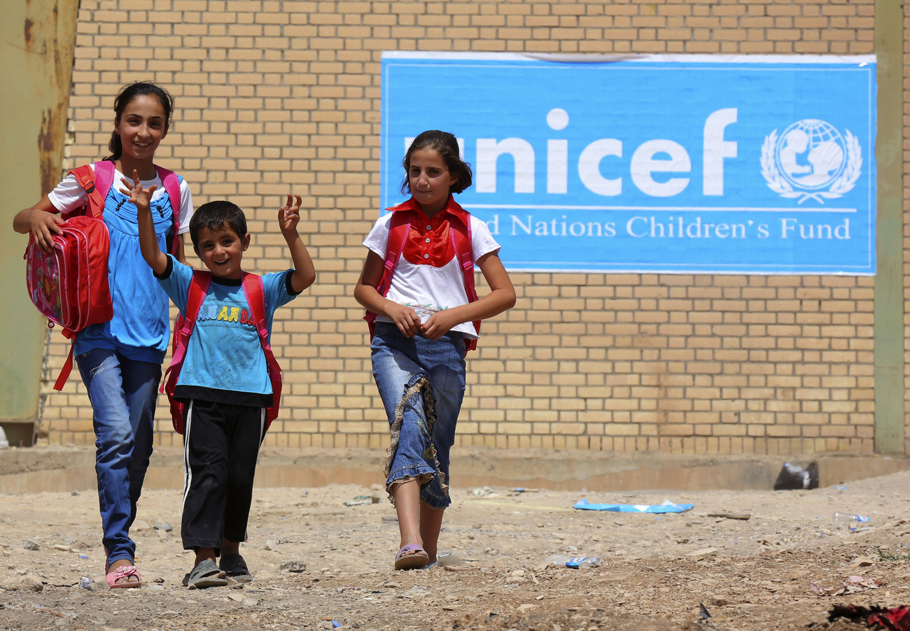 Children in Syrian refugee camp against sign for UNICEF.