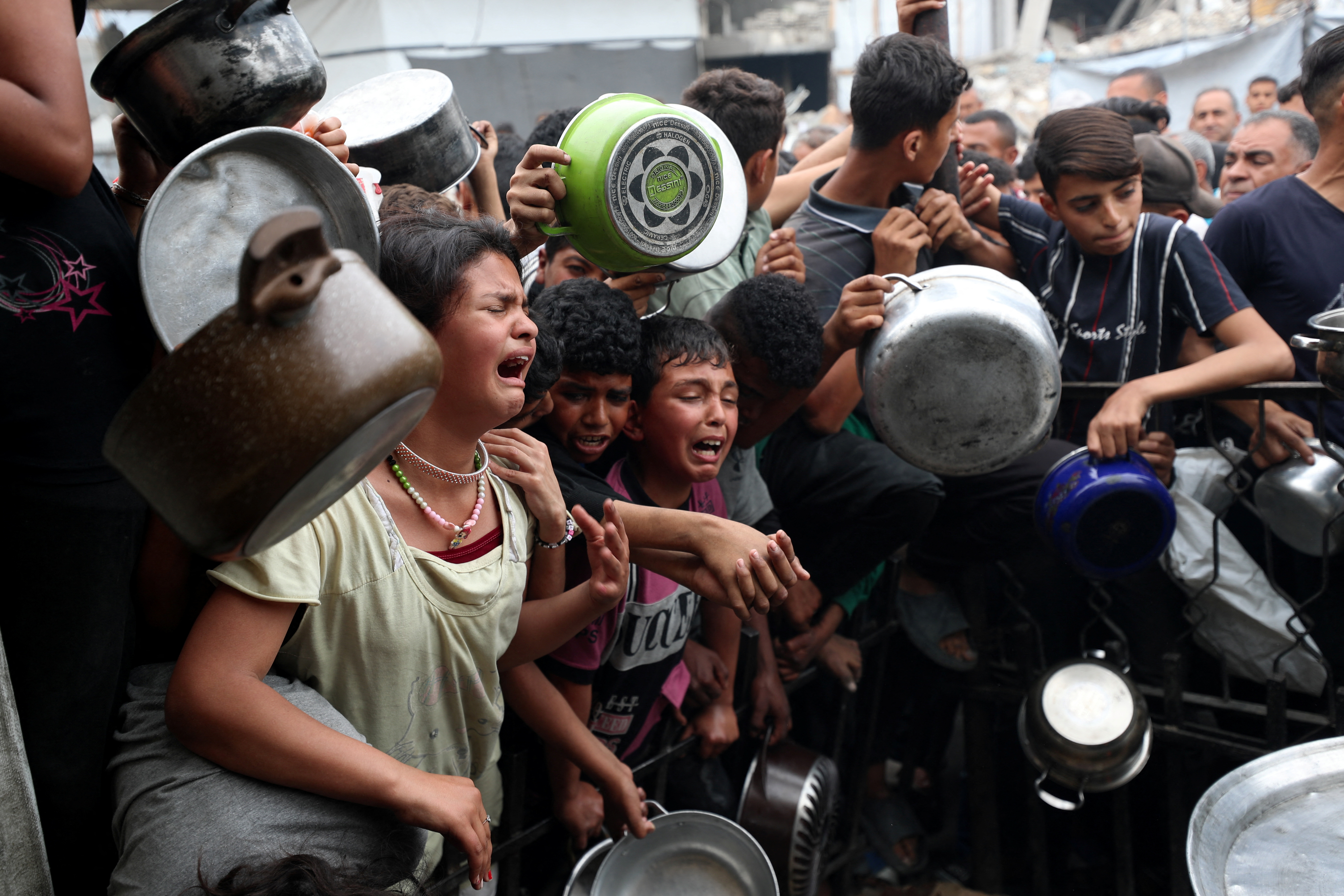 Children react as Palestinians wait to receive food cooked by a charity kitchen, in Beit Lahia, northern Gaza Strip, April 24, 2025.
