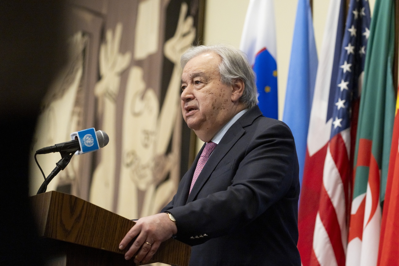 Homem falando em uma tribuna e com bandeiras por trás