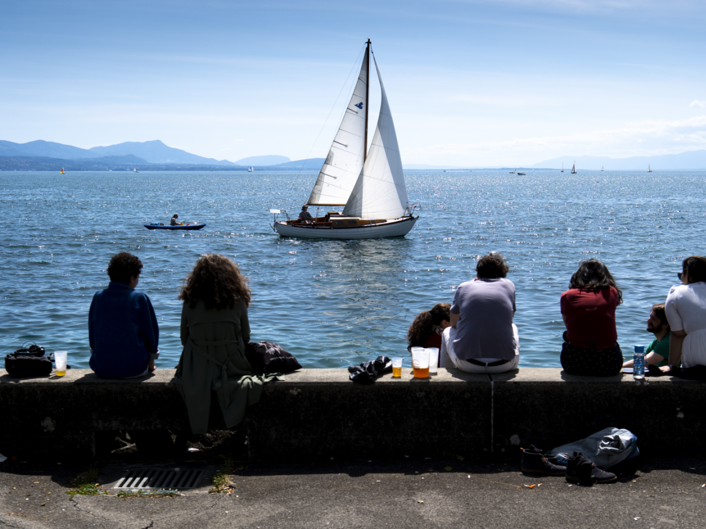 persone sedute sulla riva di un lago fotografate di spalle