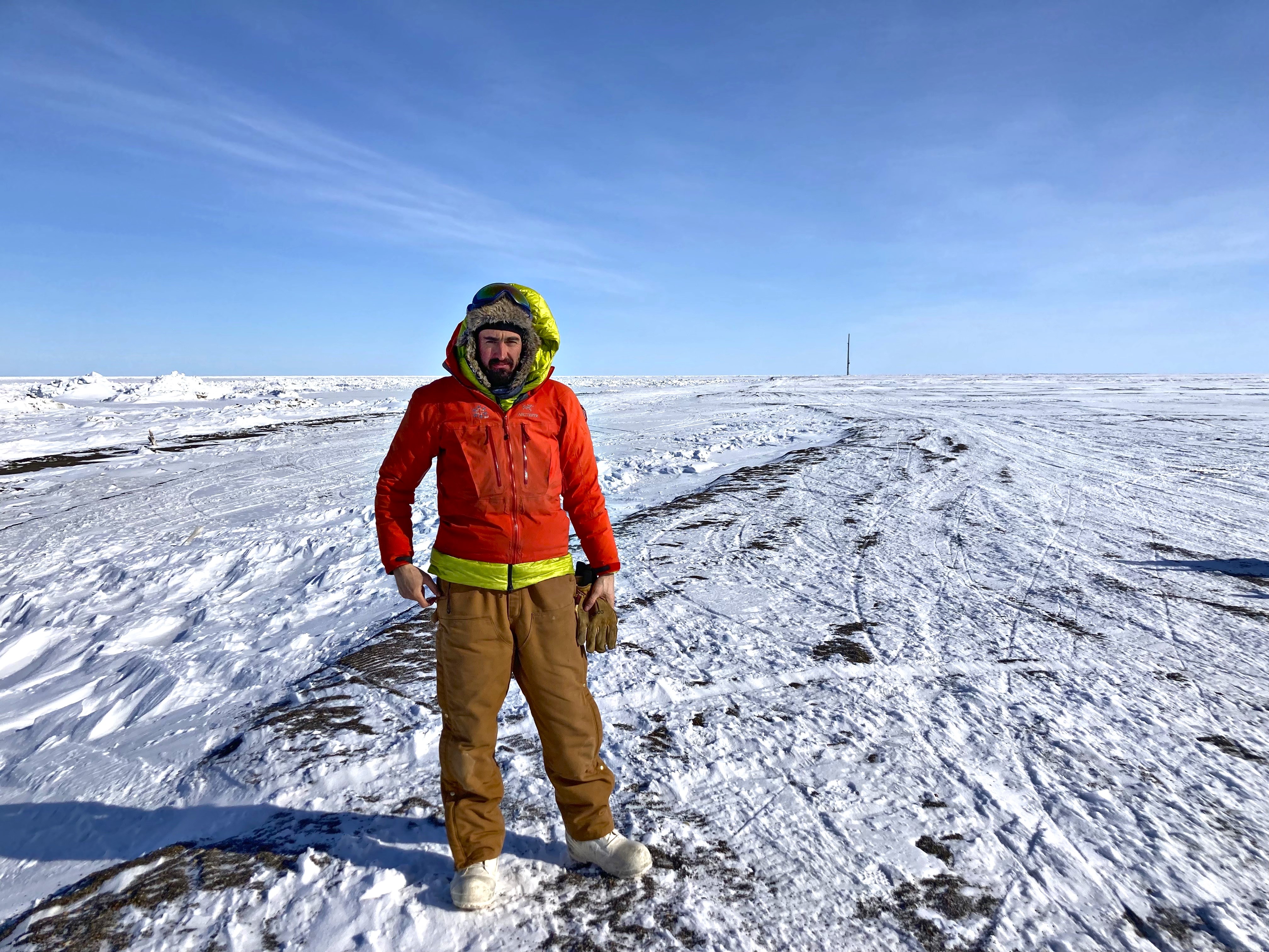 uomo con vestiti invernali in piedi su una distesa di neve e ghiaccio.