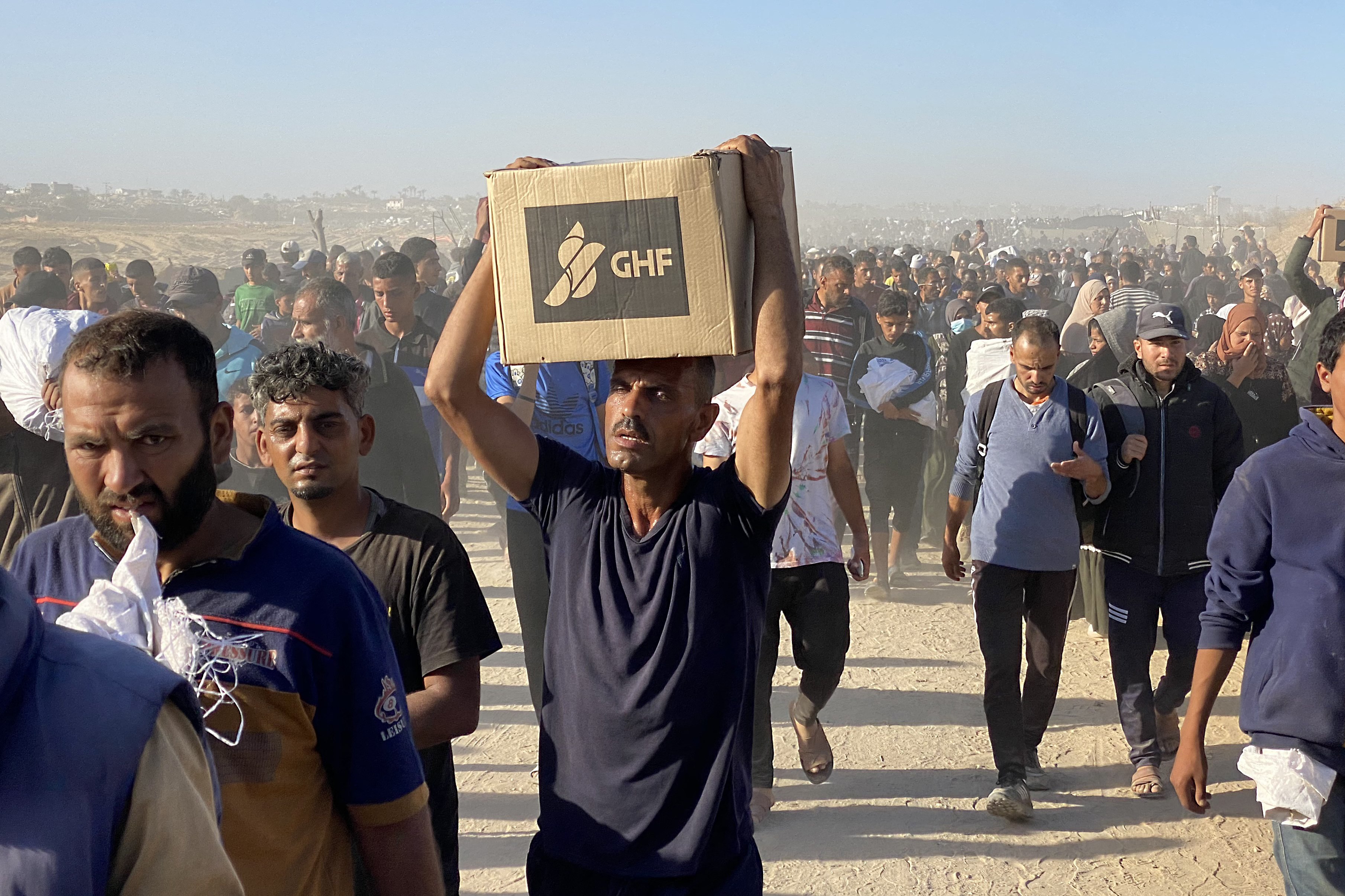 Displaced Palestinians carrying relief supplies from the Gaza Humanitarian Foundation (GHF).