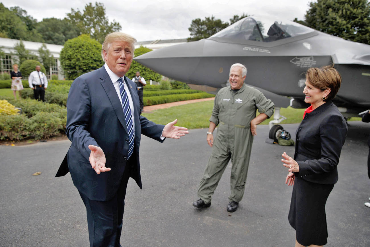 donald trump, un uomo in divisa e una donna davanti a un aereo da combattimanto