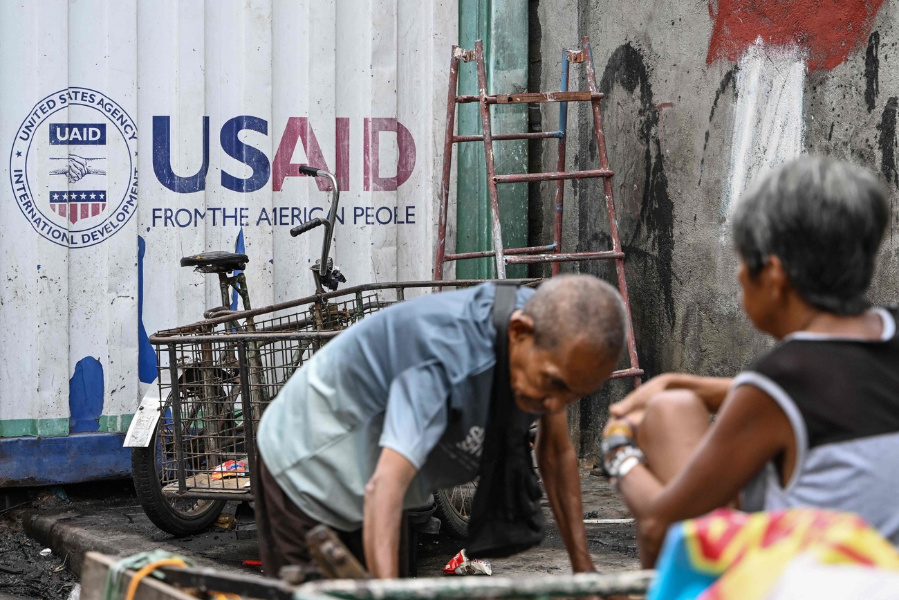 anziano inginocchiato per terra sotto il logo USAID