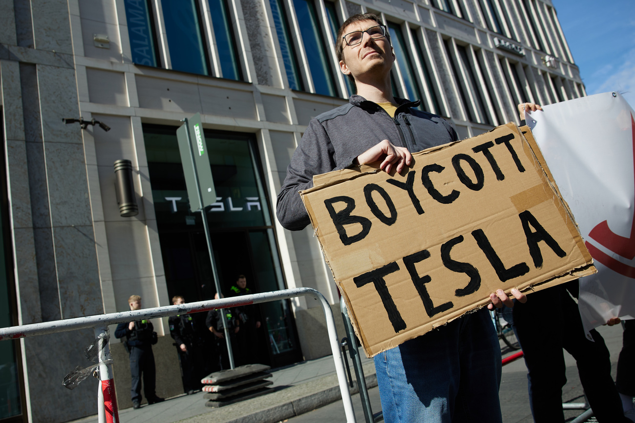 Un uomo invita con un cartello a boicottare la Tesla.