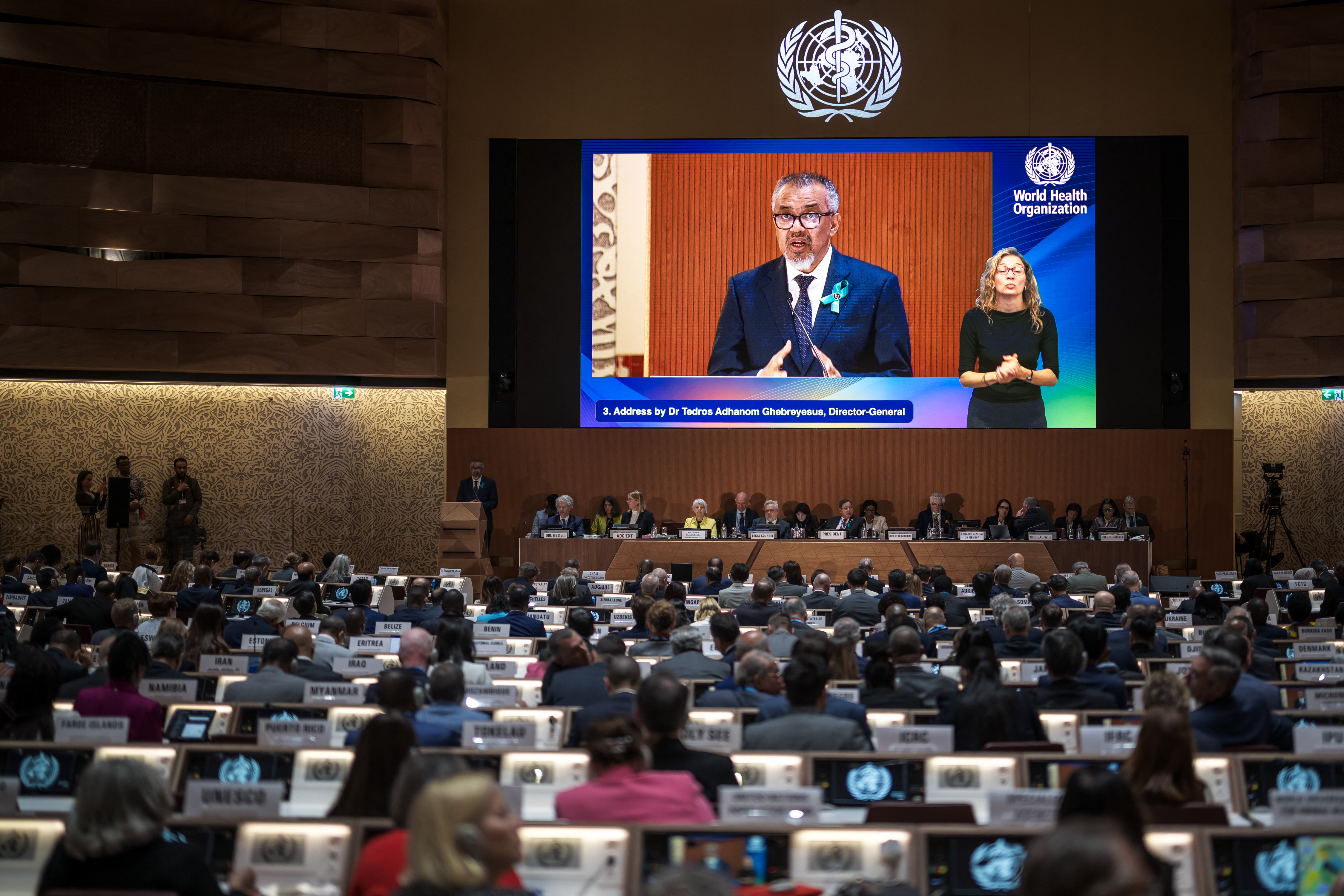 World Health Organization (WHO) Director-General Tedros Adhanom Ghebreyesus is seen on a screen delivering his report before delegates during the World Health Assembly in Geneva on May 19, 2025.