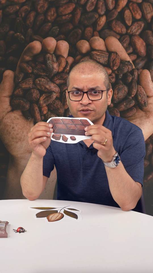 Journalist Anand Chandrasekhar sitting at a table, holding up a picture of a chocolate bar.