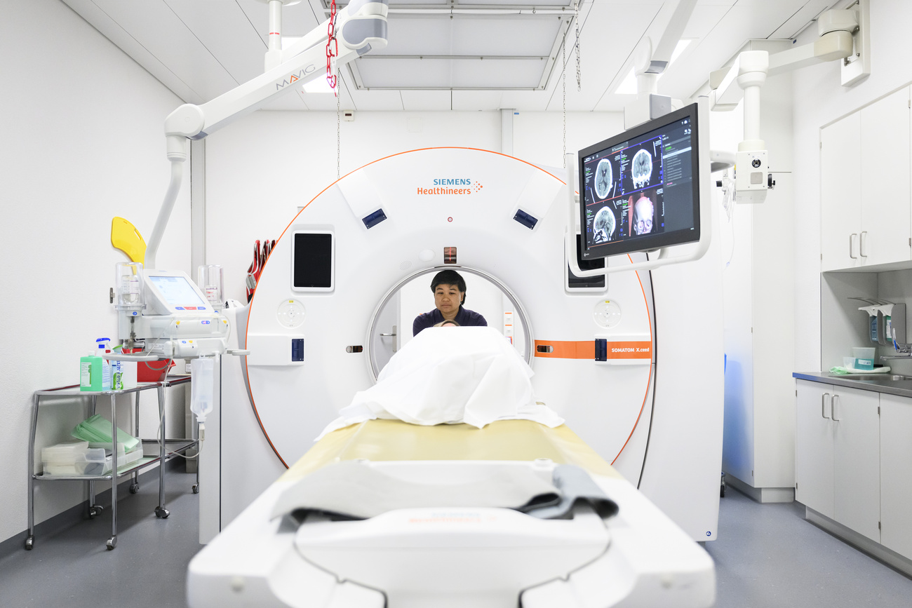 A medical personnel helps a patient in a CT scanner, used for diagnosis.