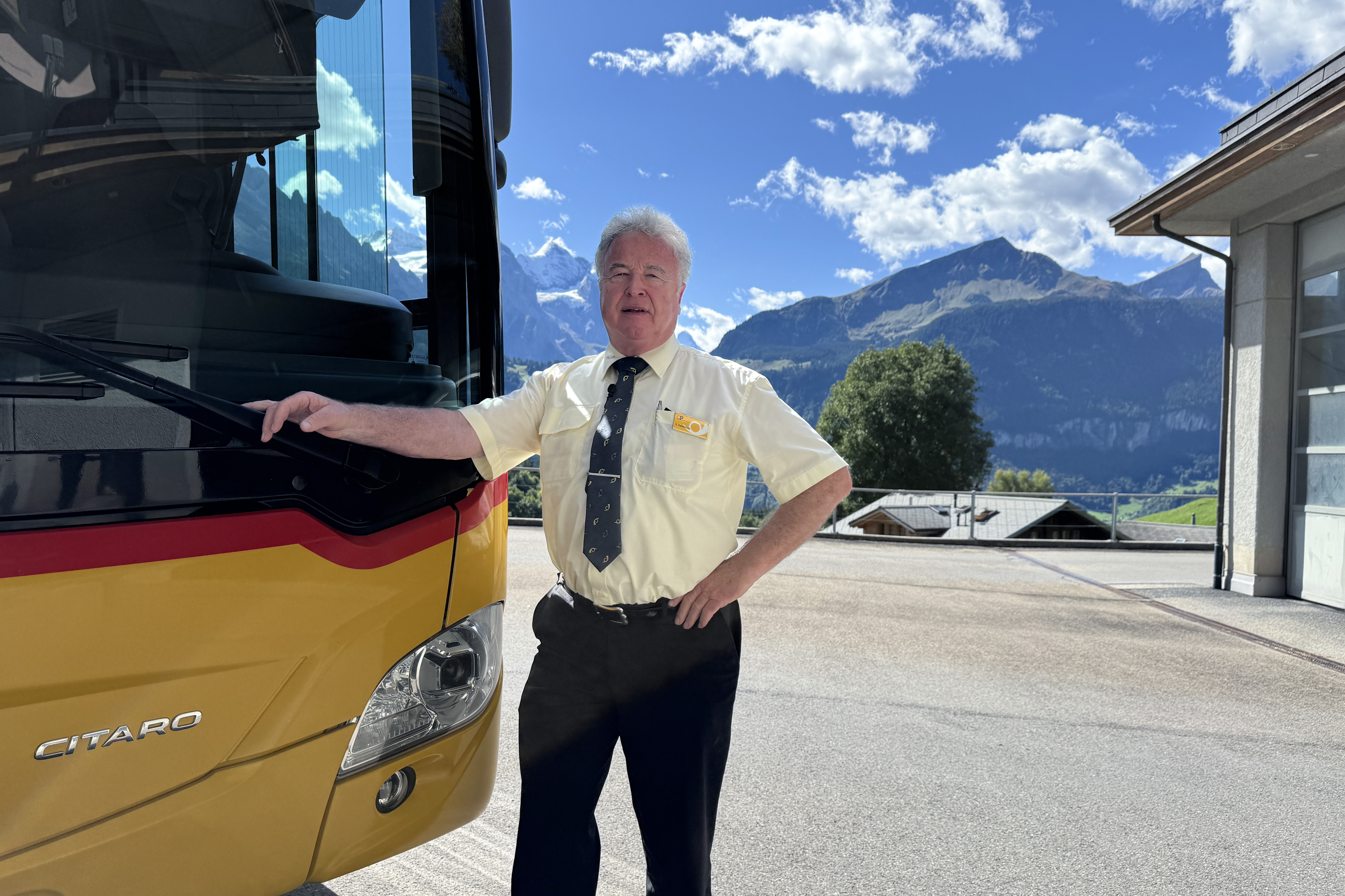 Ein Mann in Postuniform steht vor einem Postauto
