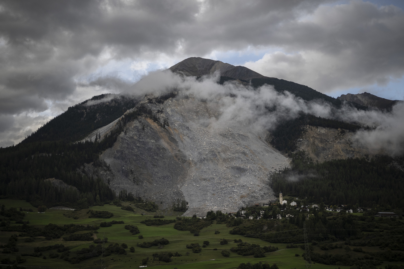 Villaggio ai piedi di una montagna sul cui versante è visibile una frana