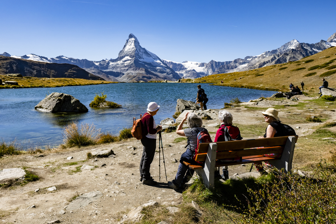 Das Matterhorn, davor ein See und Wandernde, die auf einer Bank sitzen