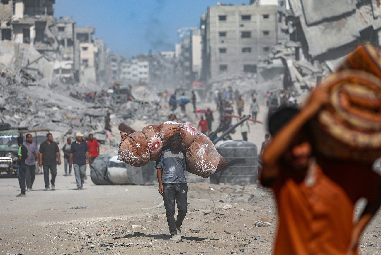 نازحون فلسطينيون يسيرون بين أنقاض المباني المدمّرة في غزة خلال التهدئة بين إسرائيل وحماس، بعد إعلان تنفيذ المرحلة الأولى من خطة السلام الأمريكية التي تشمل تبادل أسرى وانسحاب القوات وتقديم مساعدات إنسانية.