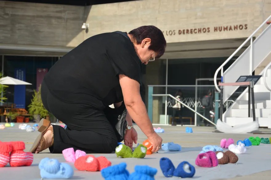 在智利圣地亚哥，一名女性在象征性的童鞋旁哀悼，这些童鞋是为了纪念被非正规收养的儿童。