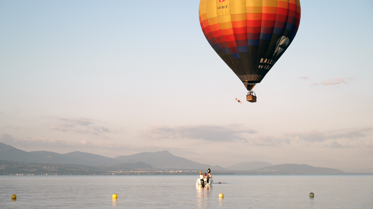 Ein Mann springt aus einem Heissluftballonkorb in einen See