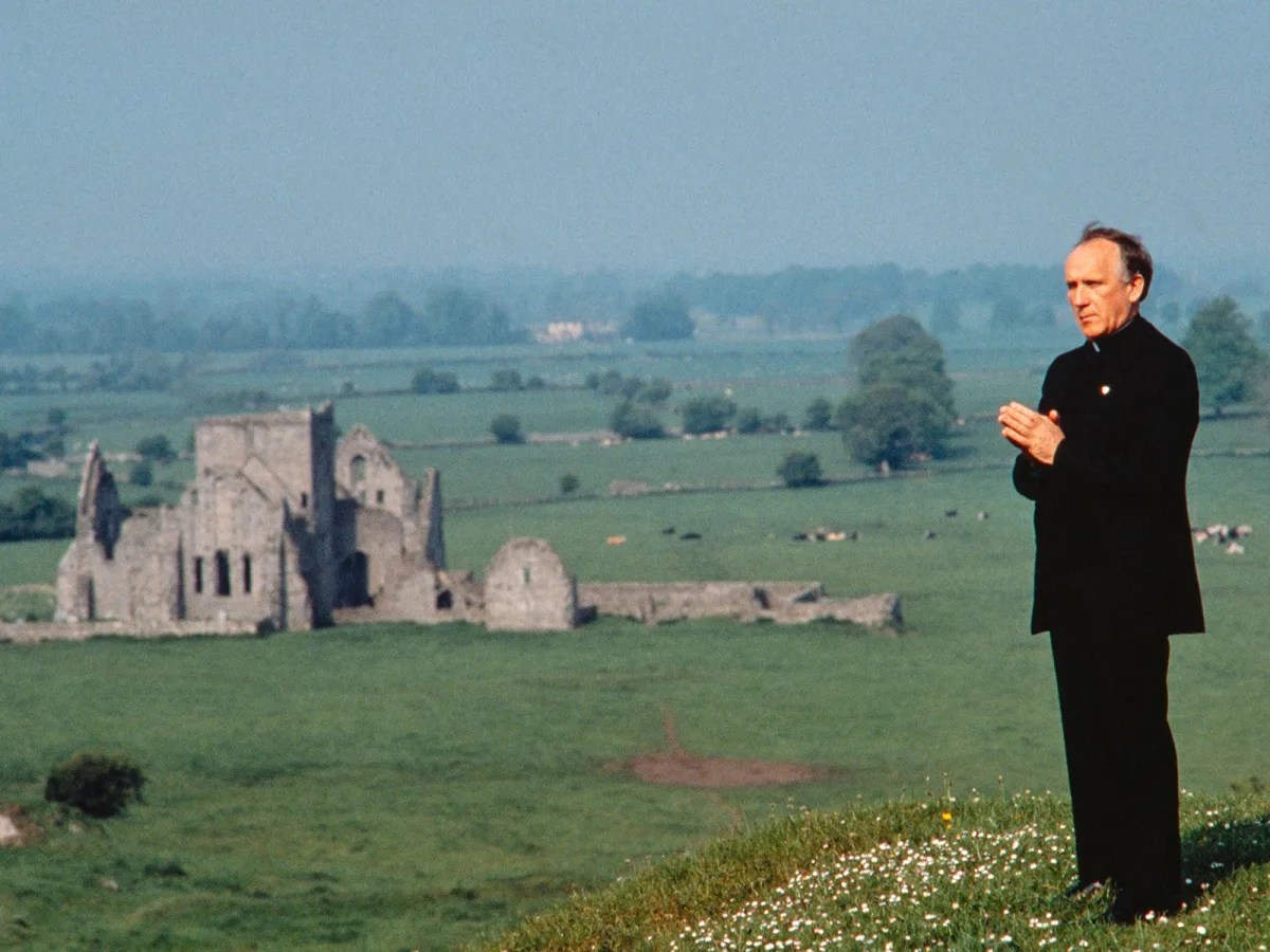 Irish priest praying standing near ruins.
