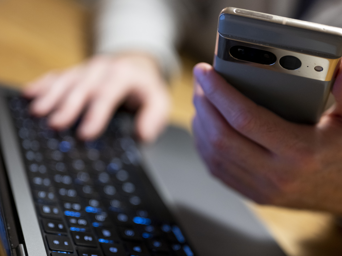 persona con smartphone in una mano scrive alla tastiera di un pc con l'altra