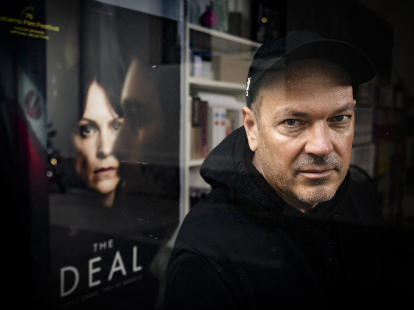 il regista romando Jean-Stéphane Bron davanti alla locandina della serie the deal