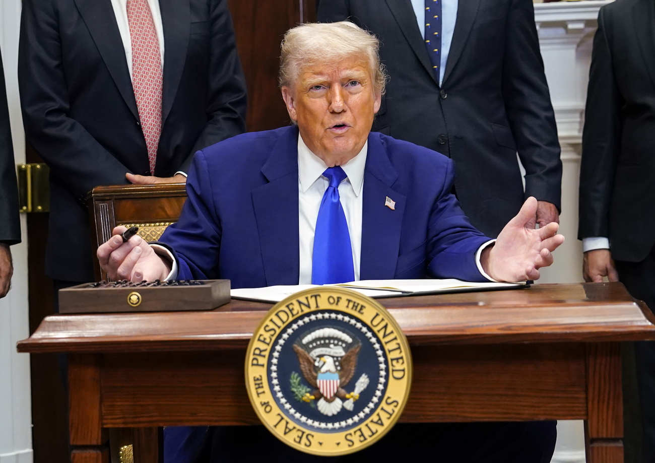 Trump sits at desk with arms open.