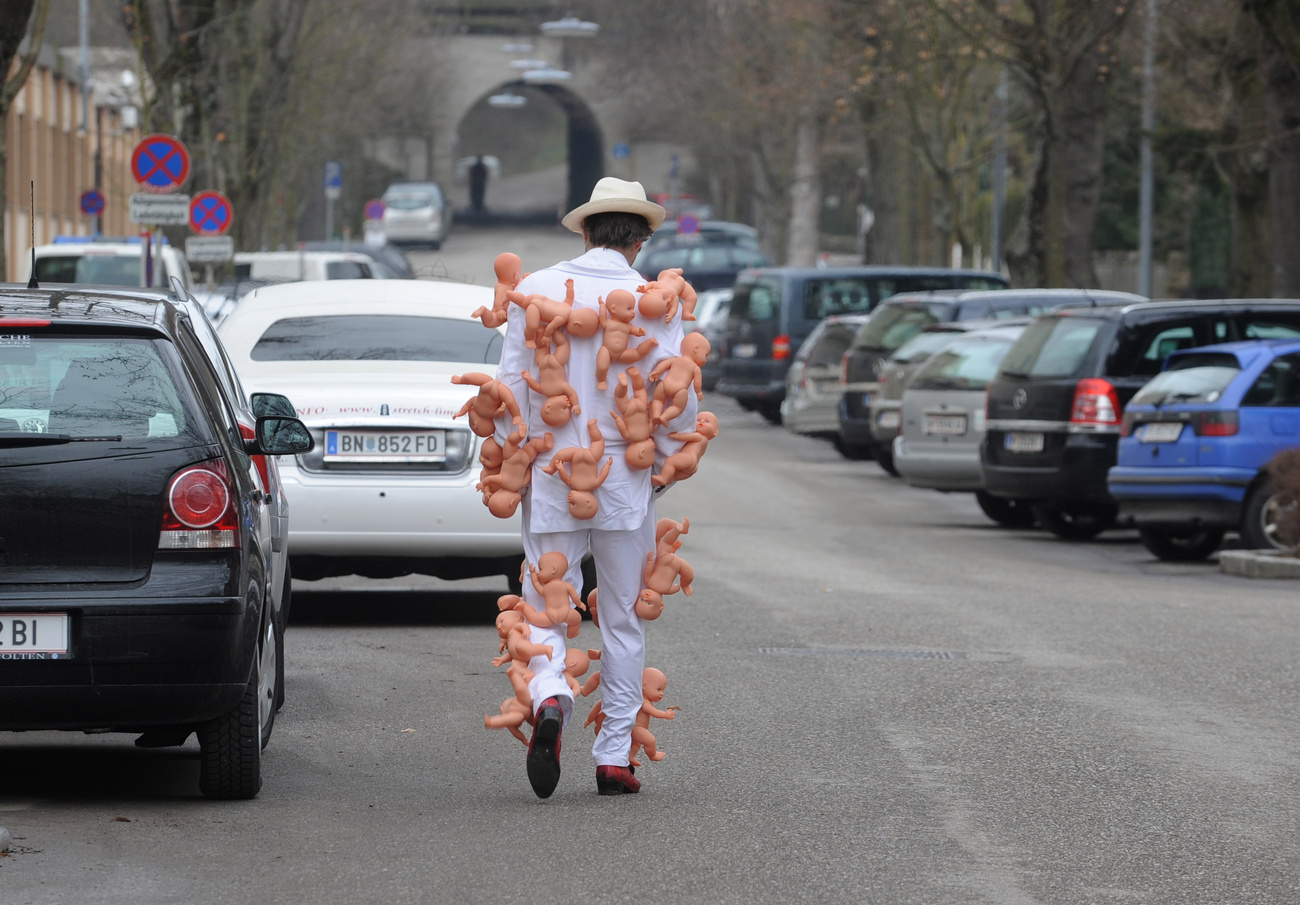 Persona in strada, di spalle, con bambole attaccate al corpo
