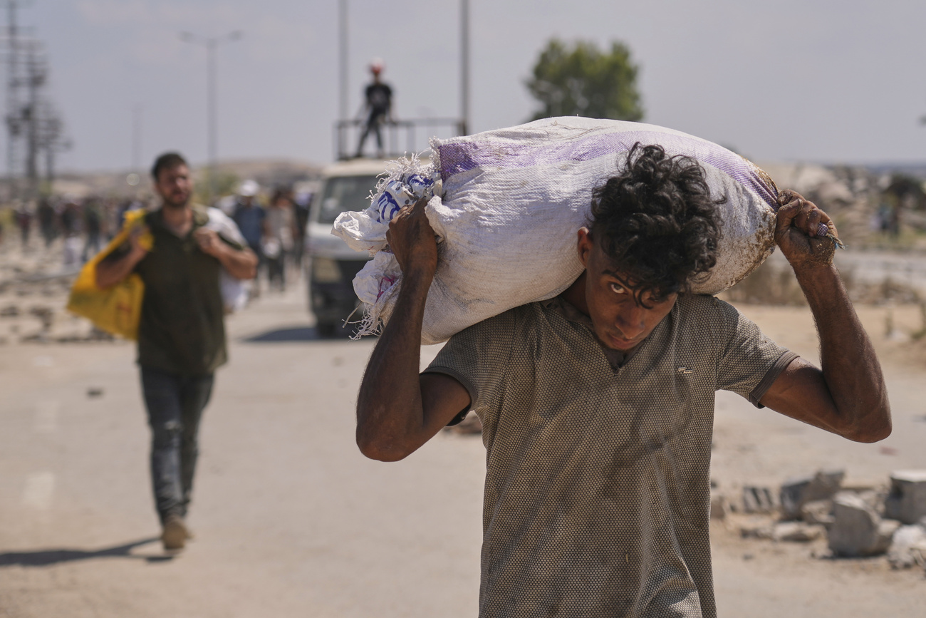 Photo of a Palestinian young man carrying a bag containing aid near a Gaza Humanitarian Foundation distribution centre.