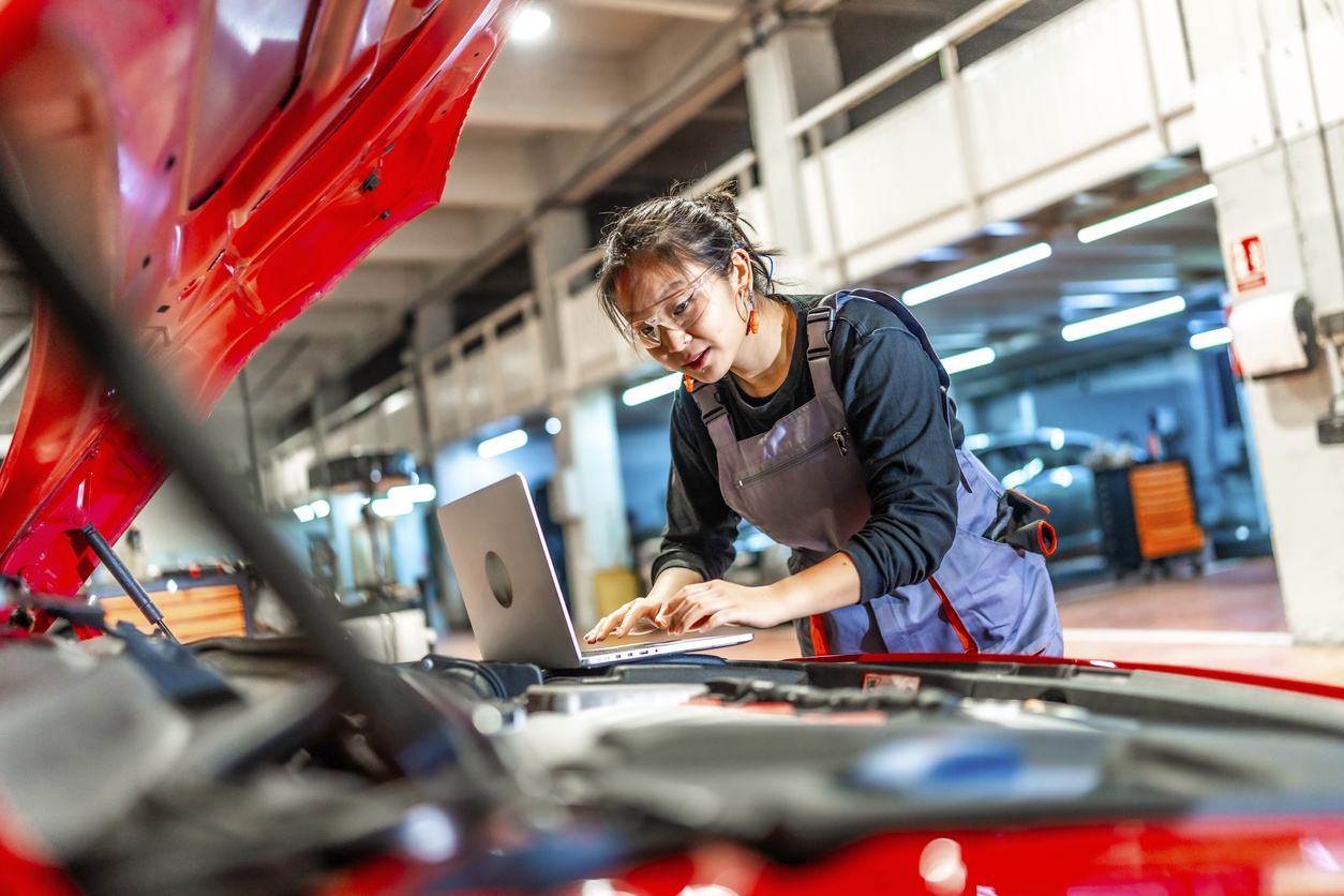 Woman at the computer in front of a car, in a workshop