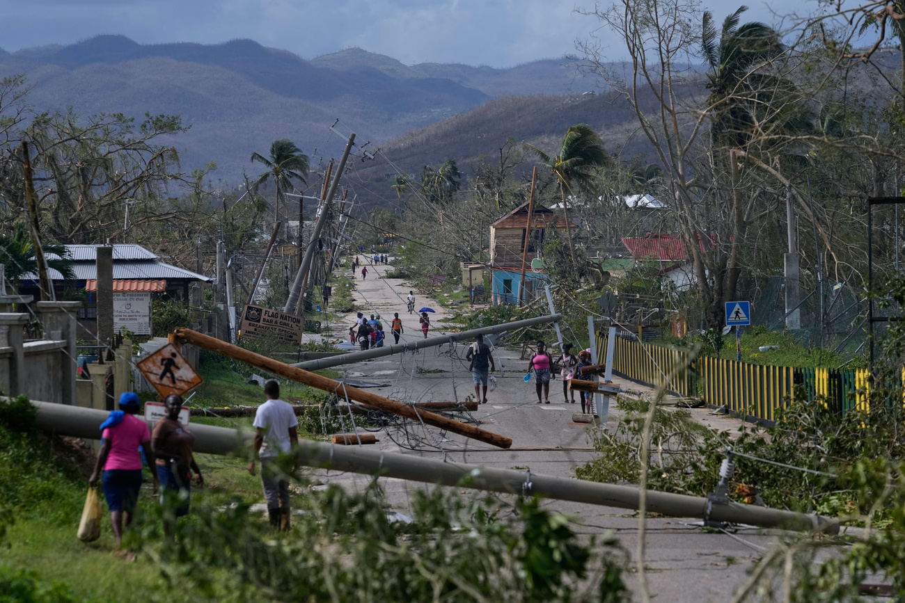 A road destroyed by the storm with fallen electricity pylons, debris and people walking along the road