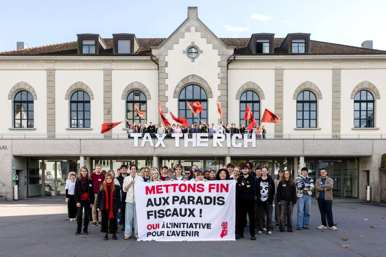 Photo of people holding a sign and "Tax the rich" sign in the background