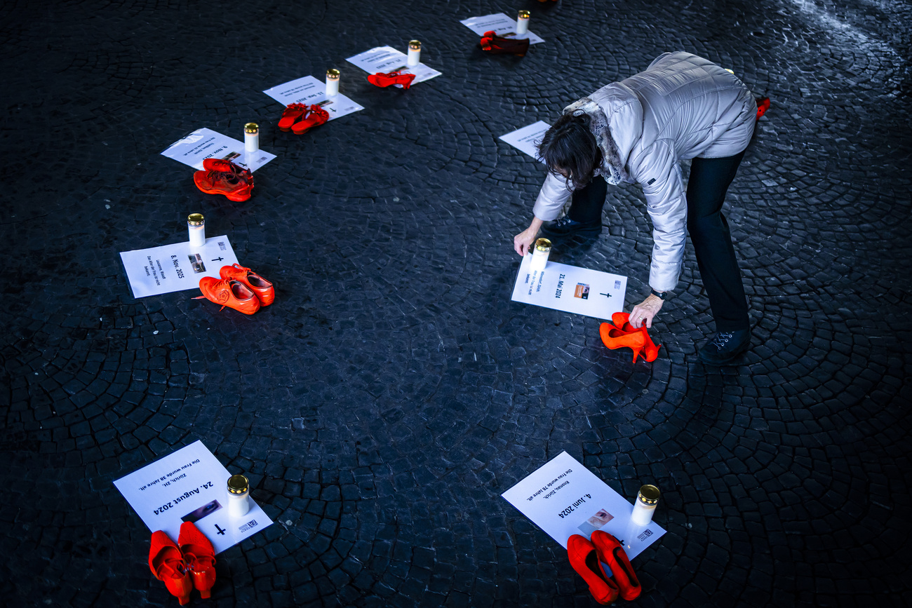 Una volontaria depone delle candele accanto a scarpe arancioni e cartelli in memoria delle vittime di femminicidio, in un'installazione alla Wasserkirche di Zurigo, durante la campagna 16 giorni contro la violenza sulle donne.
