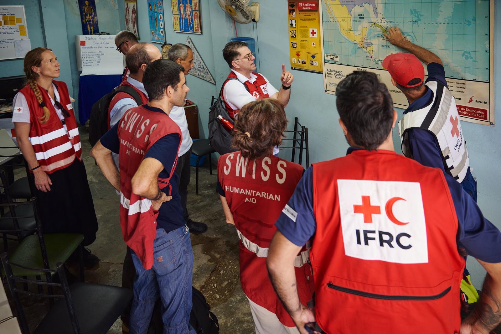 A group of humanitarian aid workers in red waistcoats have gathered around a map and are discussing it