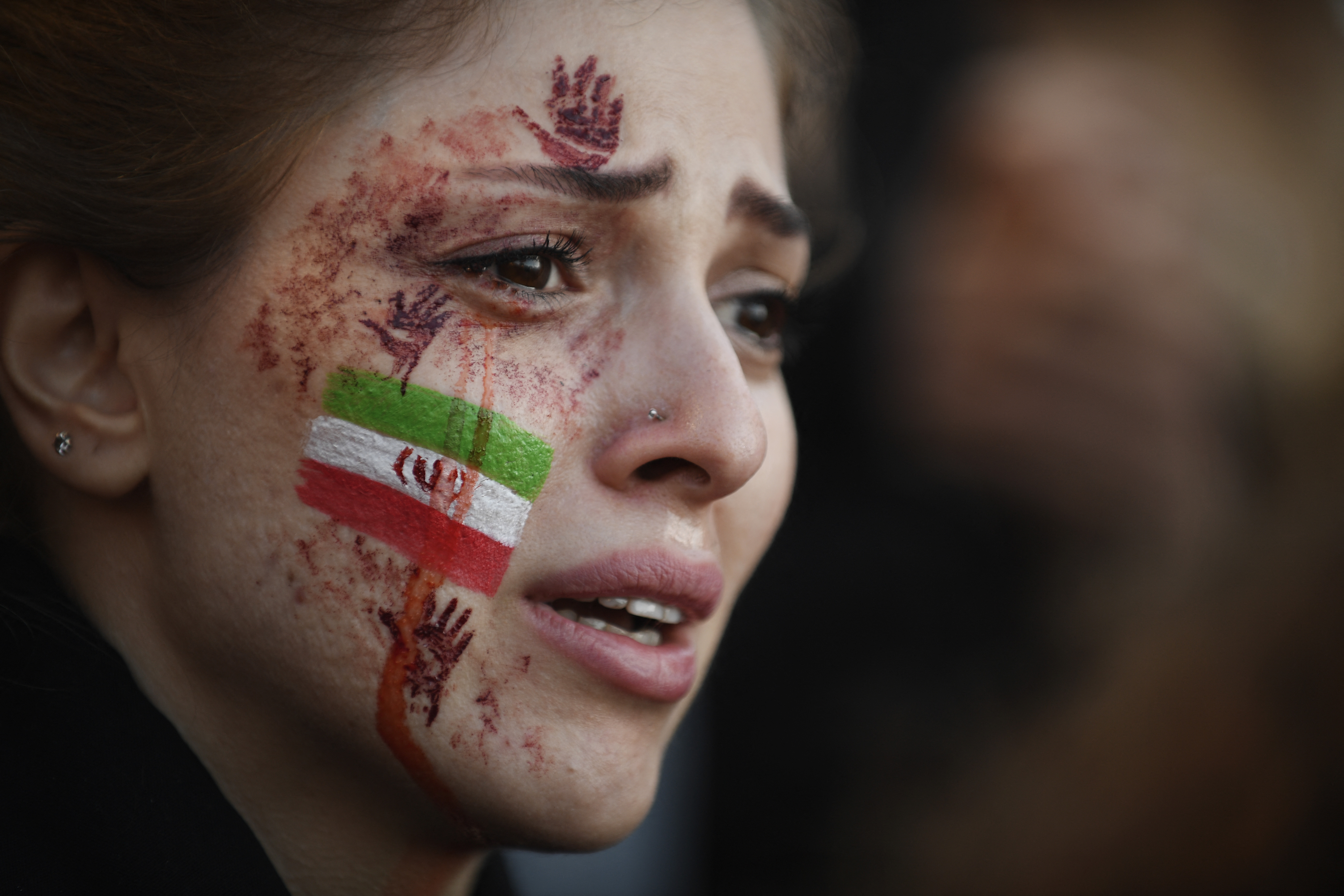 A demonstrator with an Iranian flag and red hands painted on her face attends a rally in support of Iranian protests, in Paris on October 9, 2022, following the death of Iranian woman Mahsa Amini in Iran.