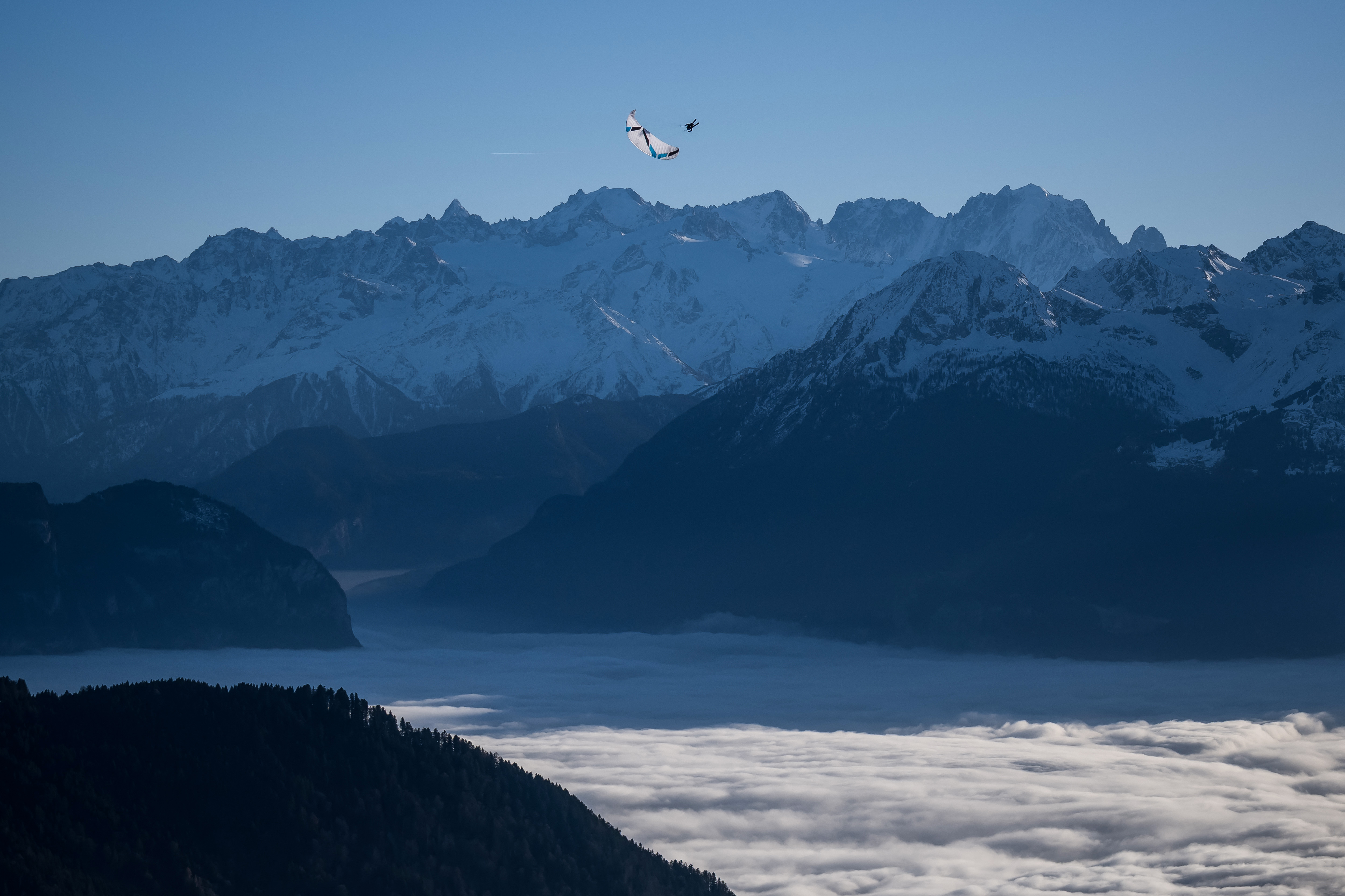 Parapendio sopra mare di nebbia, montagne sullo sfondo