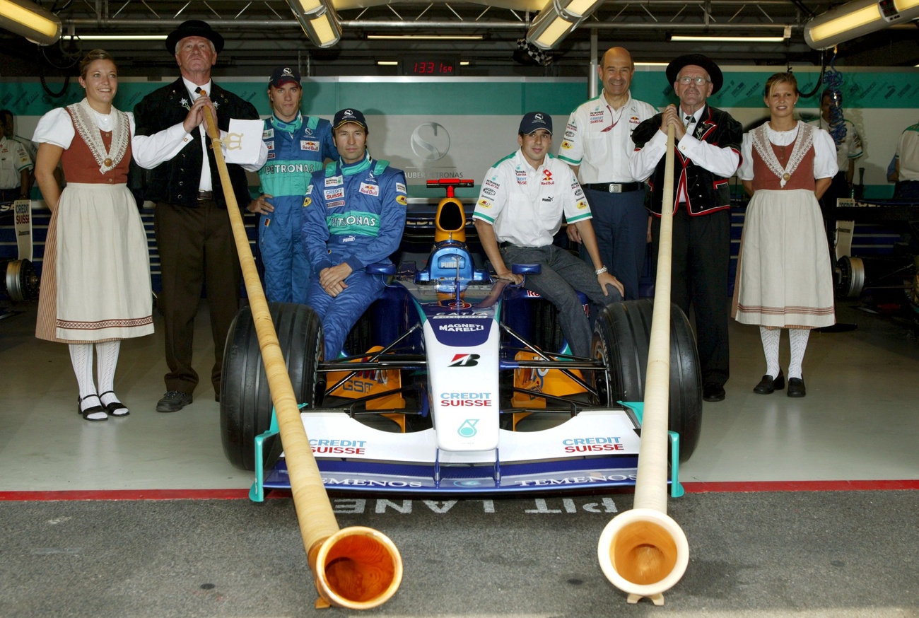 due suonatori di corno delle alpi accanto a una auto di formula uno