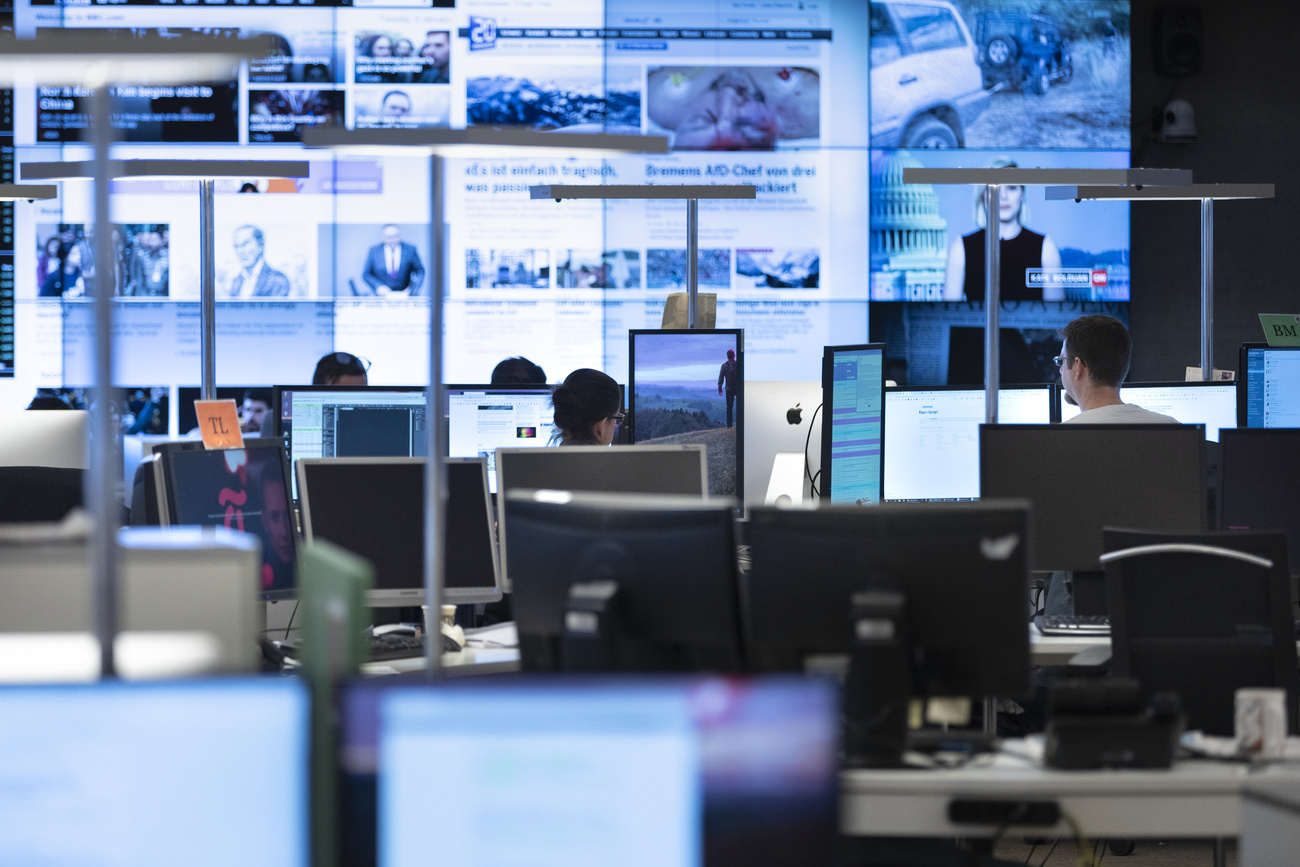 An office space with many computer screens displaying news and information and a few employees