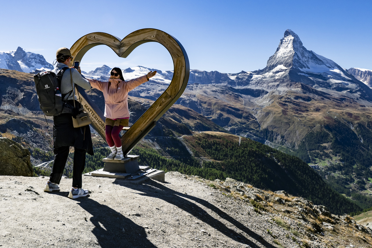 una ragazza si fa scattare una foto mentre è in piedi all'interno di una scultura a forma di cuore, sullo sfondo delle montagne innevate