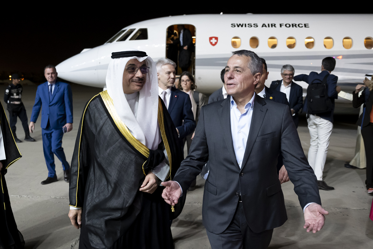 Deux hommes devant un avion "Swiss Air Force", l'un en tenue arabe traditionnelle, l'autre en costume