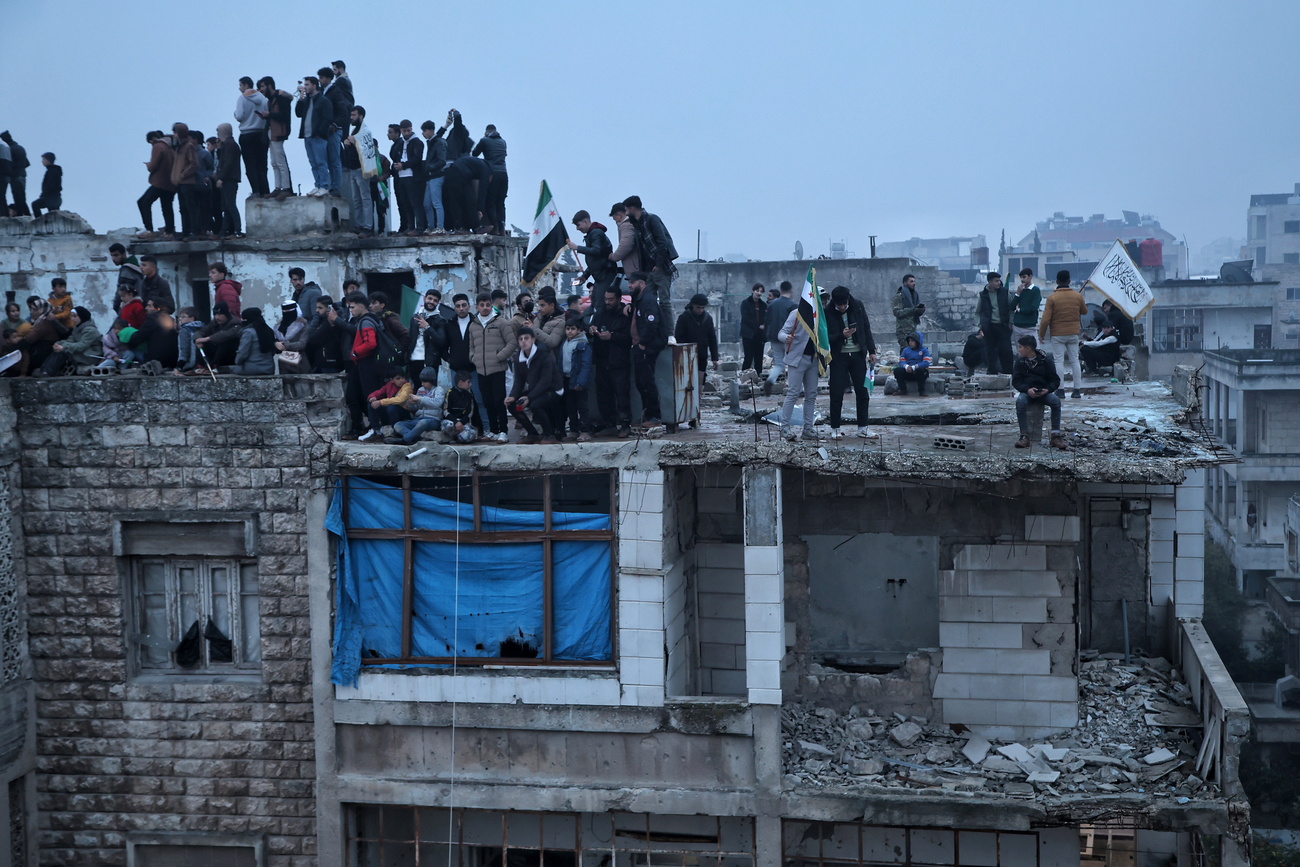 سوريون يقفون فوق مبنى خلال عرض شعبي في مدينة إدلب، احتفالًا بالذكرى الأولى لسقوط نظام بشار الأسد في 8 ديسمبر 2025.