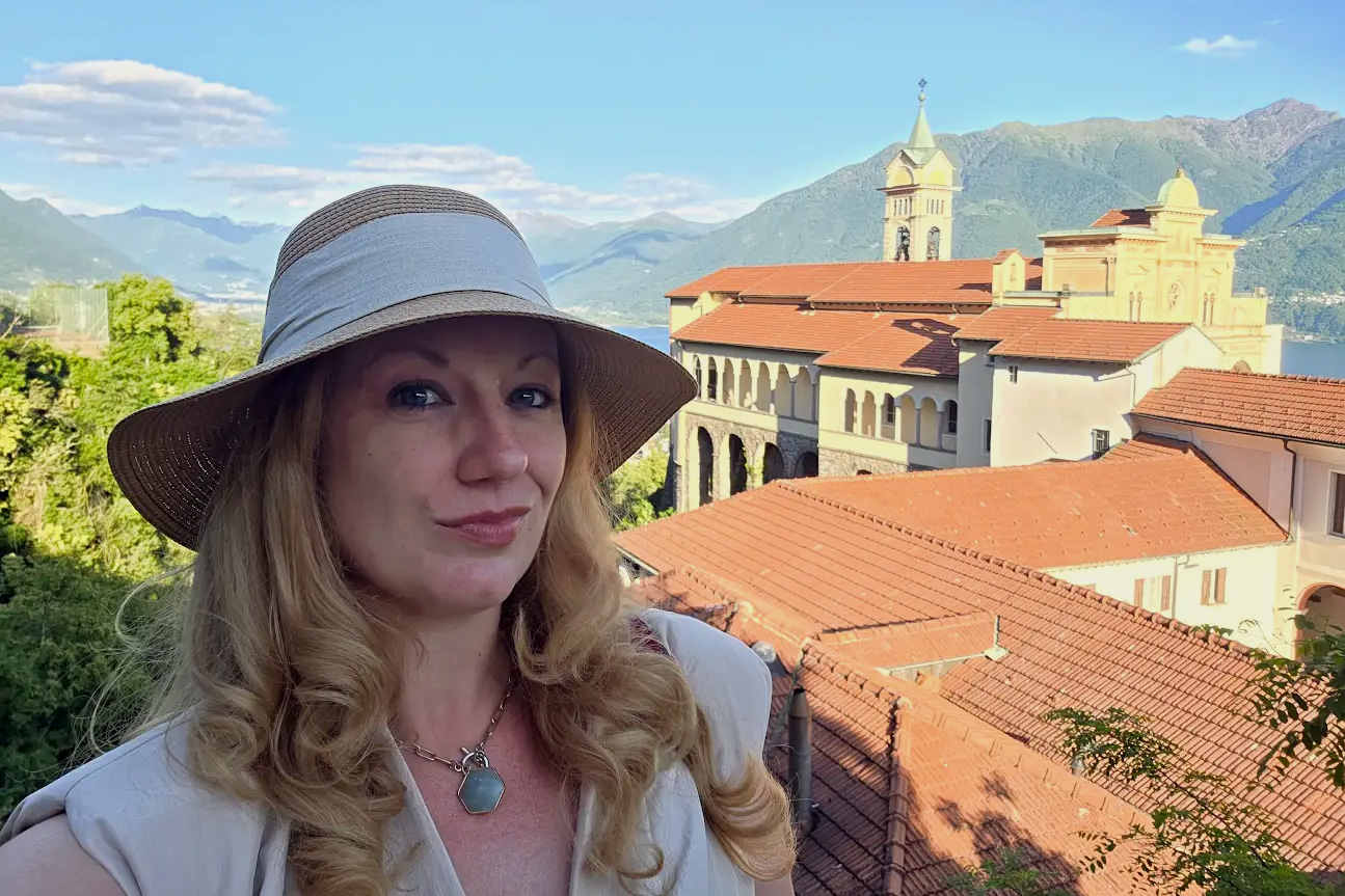 Eine Frau mit Sonnenhut, dahinter eine Kirche und der Blick auf einen See