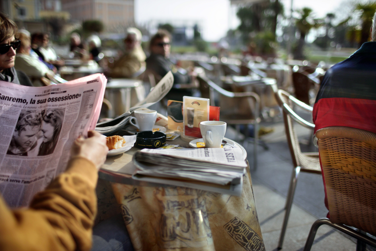 Tavolo all'aperto in un bar, una persona legge un quotidiano.