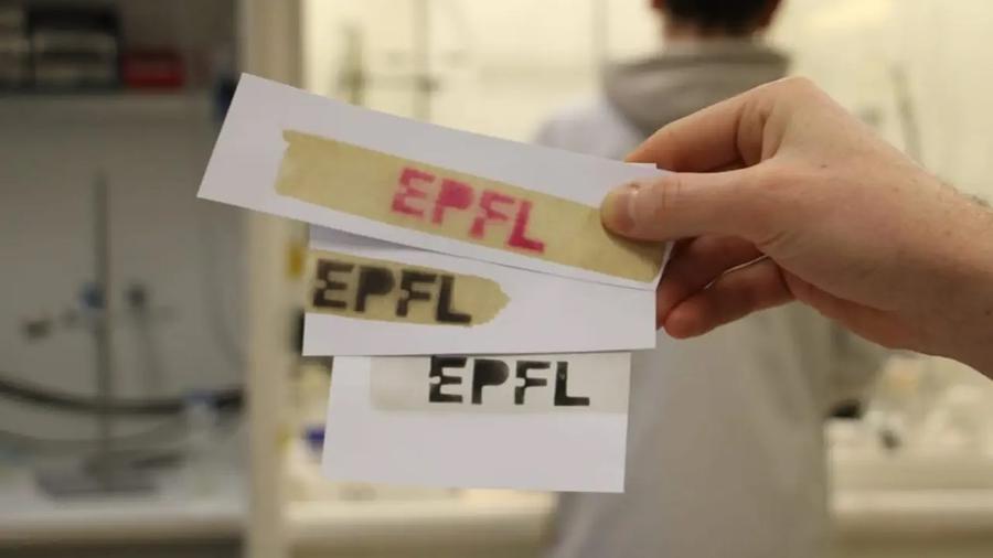 Mano regge tre pezzi di carta con scritta EPFL di diversi colori