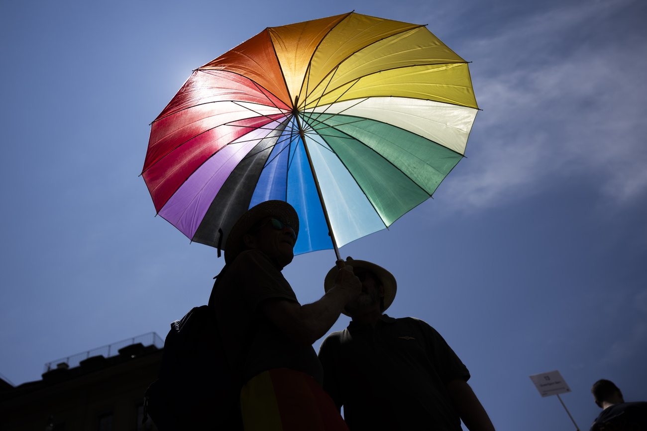 Silhouettes de personnes portant un parapluie aux couleurs de l'arc-en-ciel.